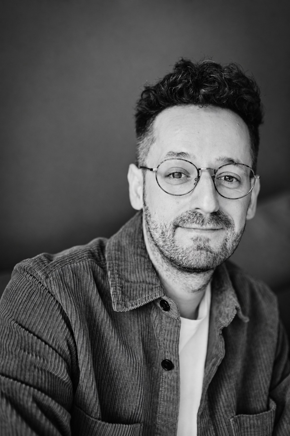 David Teloke mit runder Brille und Cordhemd, persönliches Schwarzweiß-Porträt